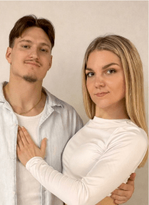 Porträt eines jungen Tanzpaares. Beide tragen helle Kleidung. Der Mann hat dunkle Haare und ein Kinnbart. Die Frau hat blonde lange Haare. Er hat seinen Arm um sie gelegt und ihre Hand liegt auf seiner Brust. Der Hintergrund ist neutral.